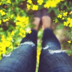 Donna in un campo di fiori gialli - dettaglio delle gambe con i jeans