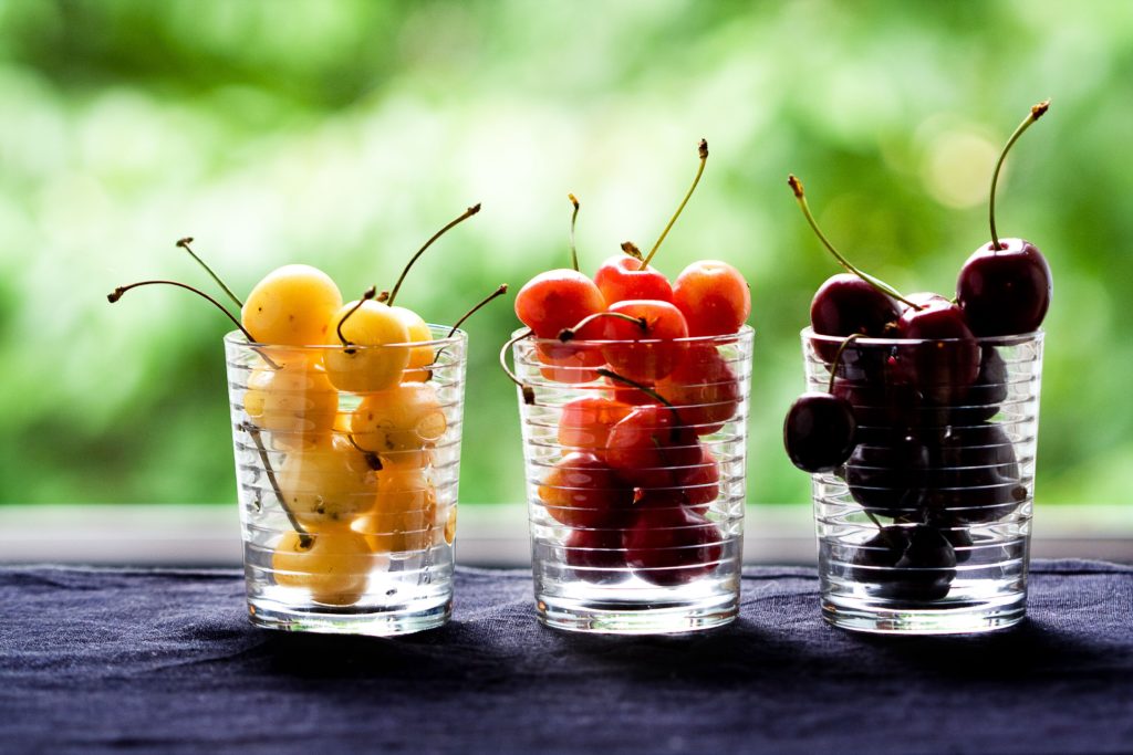 Ciliegie gialle, arancioni e nere distribuite in tre bicchieri di vetro - Frutta per il diabete consigliata